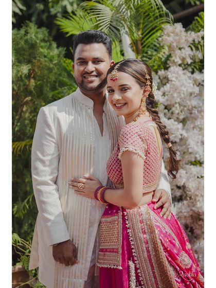 The couple shares a sweet moment. The groom's simple yet stylish white kurta with subtle striped detailing is a perfect match for the bride's vibrant outfit.