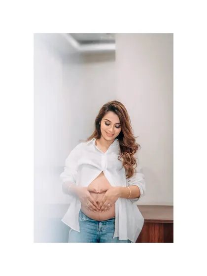 A beautiful, candid moment of a mother-to-be looking down at her baby bump with a gentle smile. This casual maternity portrait, with her in a simple white shirt and jeans, captures the pure joy and connection of pregnancy.