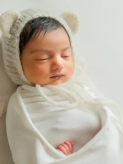 A serene close-up focusing on the baby's peaceful face and the soft texture of the bear bonnet.