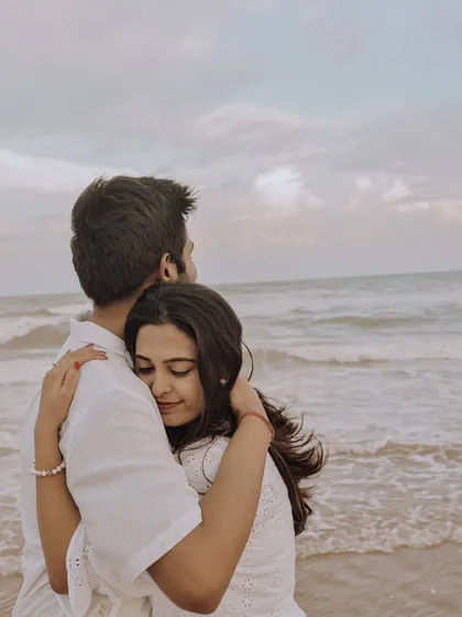 A tender embrace from behind as the couple looks out at the ocean. This intimate shot focuses on their closeness and the peaceful, romantic atmosphere of the beach.