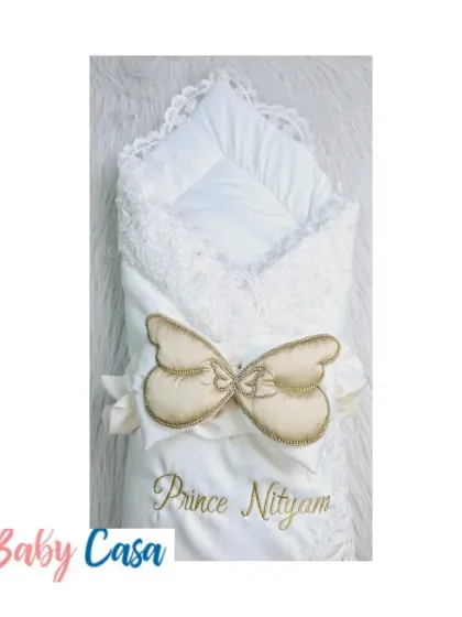 A beautiful, personalized wrap for "Prince Nityam." This elegant white wrap is adorned with a delicate lace trim and a golden butterfly motif, making it a unique and special keepsake.