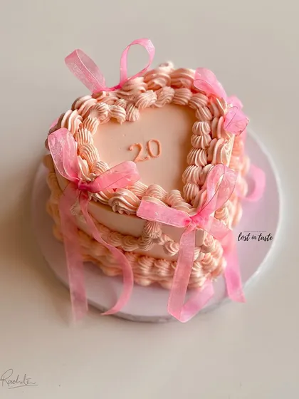 A heart-shaped buttercream cake featuring vintage Lambeth piping and delicate pink ribbons. This romantic style is perfect for birthdays, anniversaries, or just to show some love.