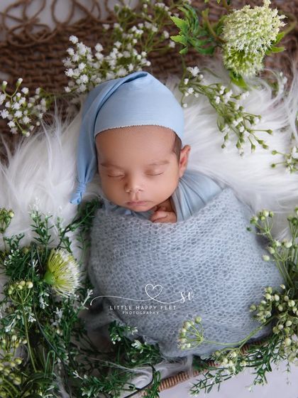 Innocence blossoms. This little prince, wrapped in a soft blue swaddle and surrounded by baby's breath, is the picture of peace and serenity.
