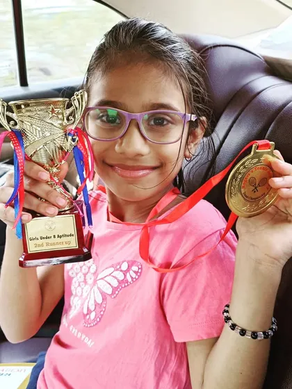 The smile of a champion. This young player proudly shows off her trophy and gold medal after a big win.
