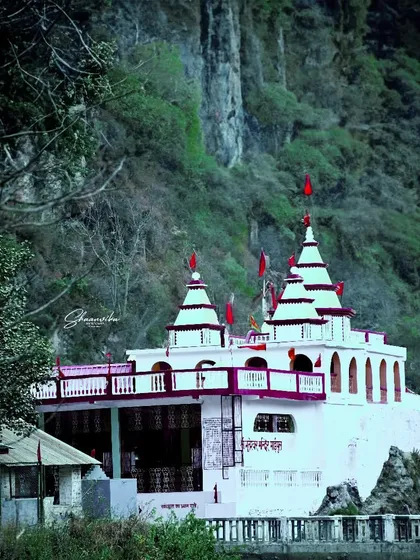 The Bhuteshwar Maharaj Maipul Temple set against a dramatic cliff face. This shot emphasizes the temple's striking white structure and its powerful location in the landscape.