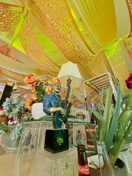 A musician statue stands among floral arrangements and a vintage lamp, part of our detailed and eclectic bar decor.