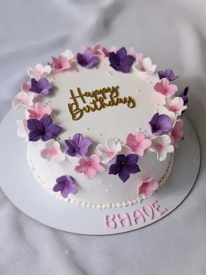 A simple floral cake, but oh so pretty. This white cake is adorned with a wreath of delicate pink and purple sugar flowers.