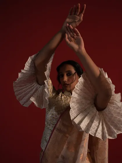 A creative close-up from the Ravissant saree shoot, this image emphasizes the architectural, pleated bell sleeves of the blouse. The model's pose and the dramatic lighting create an artistic and memorable fashion shot.
