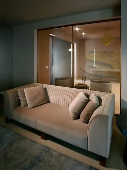 A comfortable sofa in a neutral tone, with a view into an adjoining room through a large glass partition, showcasing the home's fluid, open-plan design.