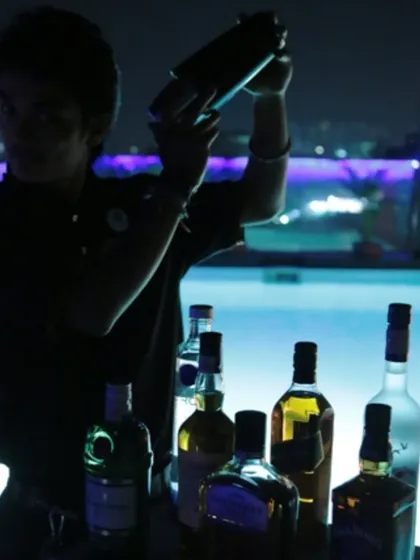 A bartender shaking up cocktails against a poolside backdrop at night. We can set up our mobile bar anywhere, from a terrace to a poolside, bringing a cool, professional vibe to your party.