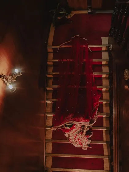 An artistic shot of the bride's stunning red lehenga, elegantly draped over a staircase. This highlights the beauty and grandeur of the wedding attire itself.