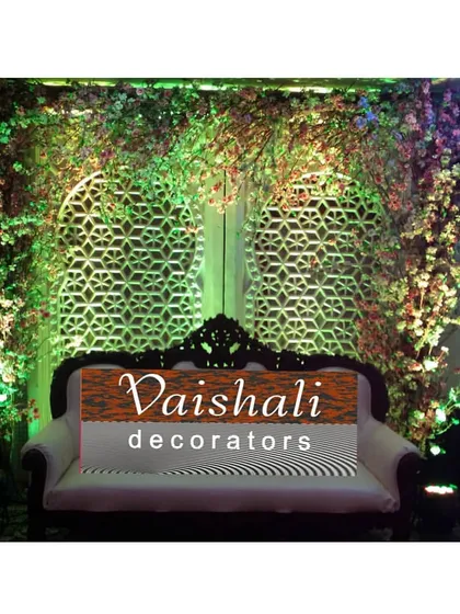 A unique stage design combining nature and tradition. This rental includes a comfortable sofa, intricate jaali panel backdrops, and lush green floral arrangements illuminated with spotlights.