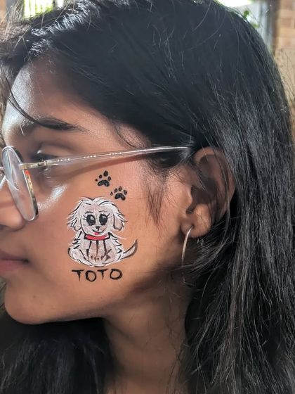 A custom pet portrait. This girl wanted her dog "Toto" painted on her cheek, complete with paw prints.