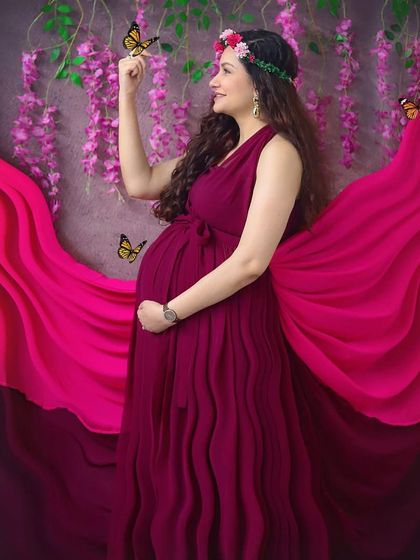 Feeling like a goddess in this whimsical studio setup. The flowing magenta gown, flower crown, and magical butterflies create a truly enchanting maternity portrait.