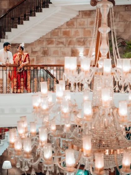 A grand wedding portrait taken from a low angle, featuring a massive chandelier that adds a sense of opulence and scale to the venue.