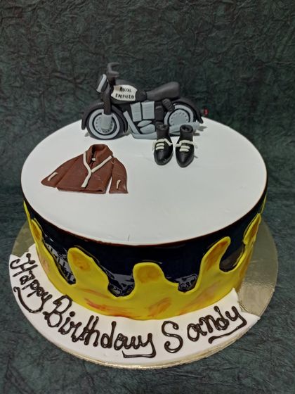 A Royal Enfield Bullet-themed cake for a bike lover. The design features a miniature fondant bike, a leather jacket, and boots on top of the cake.