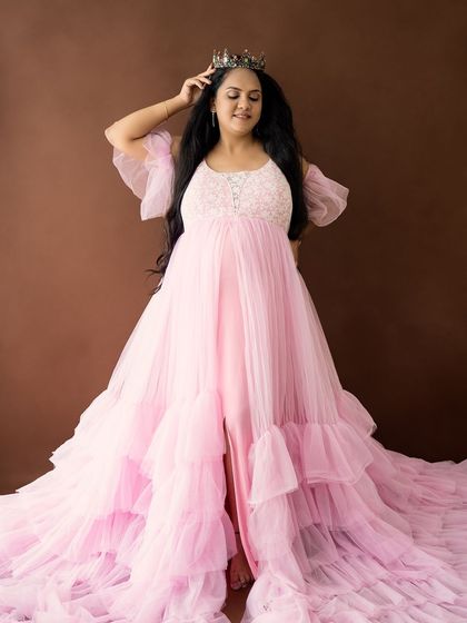 A royal portrait of a mom-to-be wearing a crown with her pink gown, looking down with a gentle smile.