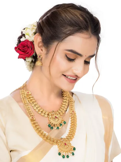 A model showcases a traditional gold temple jewellery set, including a layered necklace and jhumkas. The styling with a flower-adorned bun and classic saree is ideal for heritage brands targeting the bridal market.
