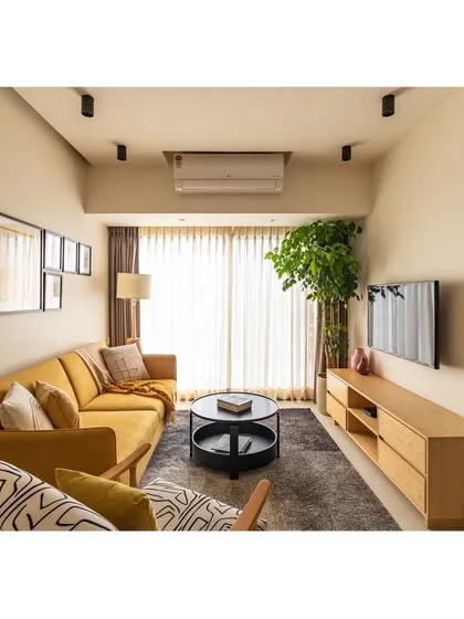 The full view of the living room, with its mustard sofa, abstract accent chair, and simple, functional TV console. The space is bright, airy, and full of personality.