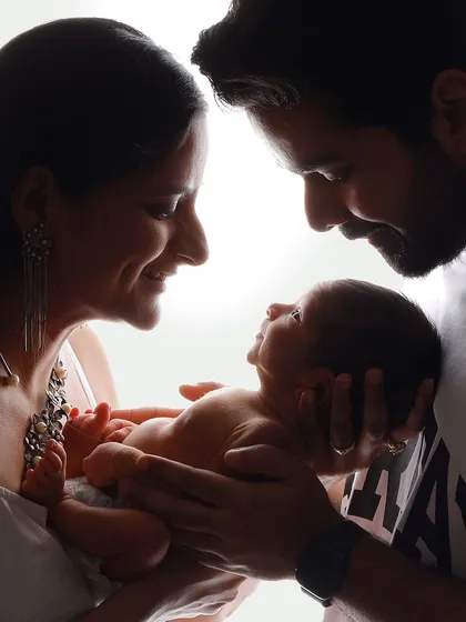 An unswaddled baby held securely in their parents' hands. This silhouette shot is powerful because it shows the baby's natural form and the parents' gentle, protective hold.