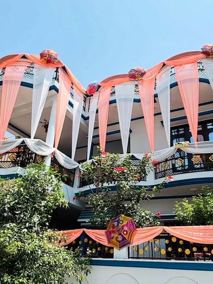 An elegant house decoration using pastel peach and white drapes. The balconies are adorned with drapes and Rajasthani umbrellas, giving the house a sophisticated and festive appearance.