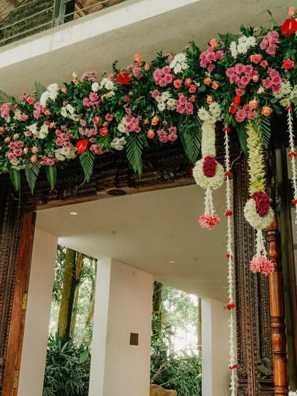 A beautiful floral garland decorating the entrance of a wedding venue, combining pink and red flowers with traditional hanging elements.