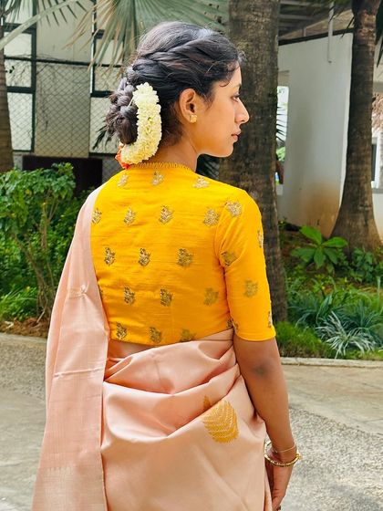 A side profile showing the fit of the embroidered yellow blouse and the soft drape of the peach silk saree.