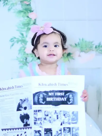 A baby girl holding a personalized "First Birthday" newspaper.