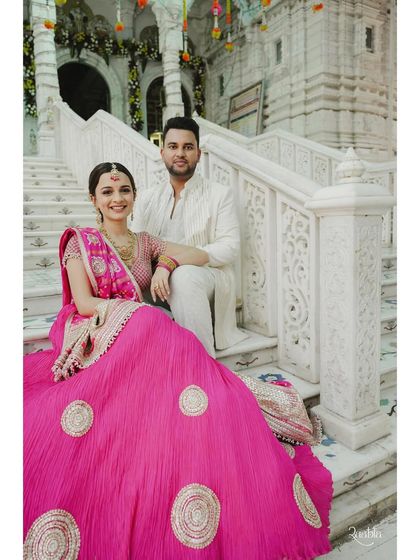A beautiful portrait of the couple for their pre-wedding pooja. The bride is vibrant in a custom Rani Pink lehenga from Faabiiana, complemented by the groom's elegant white custom kurta.