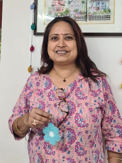 A smiling crafter with her finished blue flower charm, ready to be used as a keychain or decoration.