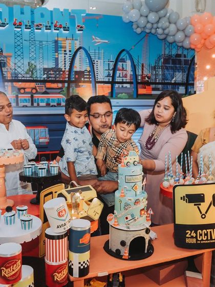 The cake-cutting ceremony at Sidhant's party, with the whole family gathered around the amazing construction-themed cake and dessert table.