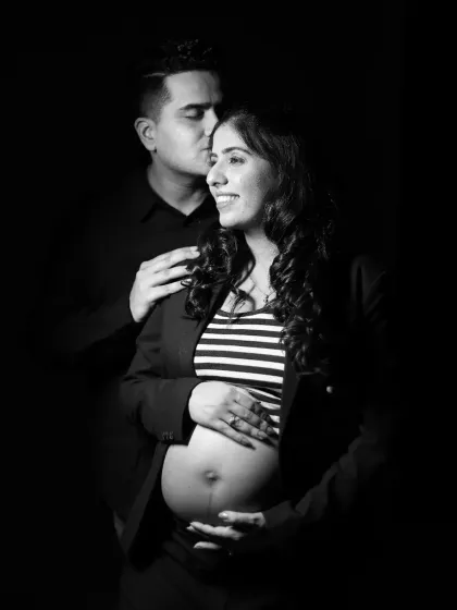 A dramatic low-key black and white portrait of a couple. The partner kisses the mother-to-be's head in this intimate and artistic shot.