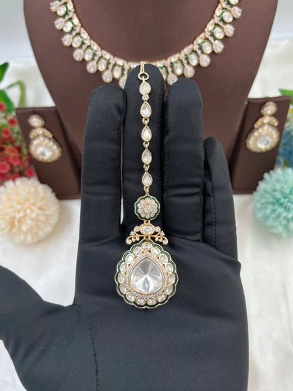 The Amaya Premium Moissanite Kundan Necklace. This set is distinguished by its large central pendant and matching earrings, featuring fine Meenakari work. It is available with red or green accents.