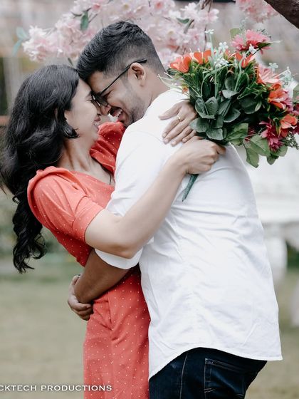 A joyful and romantic embrace, with the couple laughing and holding a bouquet of flowers.