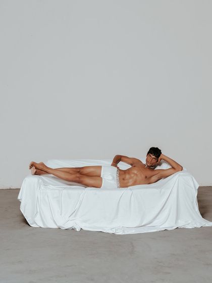 A minimalist, full-body shot for the same campaign. The composition uses negative space to create a sense of calm and intimacy, drawing the viewer's eye to the relaxed form of the model.