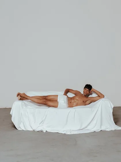 A minimalist, full-body shot for the same campaign. The composition uses negative space to create a sense of calm and intimacy, drawing the viewer's eye to the relaxed form of the model.