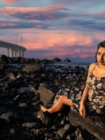 A thoughtful pose against the rocky shore of Mumbai. The soft sunset colors and the iconic Sea Link create a dreamy and cinematic fashion photograph.