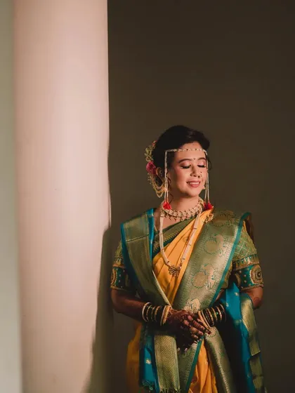 A dramatic and artistic portrait. The lighting creates a beautiful mood, highlighting the bride's silhouette and the rich colors of her traditional Nauvari saree.