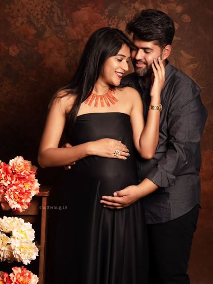 An intimate moment between expecting parents, both dressed in elegant dark tones. The mom-to-be's black satin gown and the couple's gentle embrace make this a sophisticated and emotional maternity portrait.