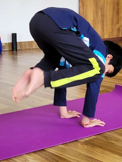 A young boy attempts crow pose, showing great determination. My classes are a safe space for kids to challenge themselves and celebrate every effort, not just the final pose.
