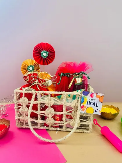 This rustic woven bag is a chic and eco-friendly option for a Holi hamper. It's filled with colorful potlis and gulal, and decorated with festive paper fans.