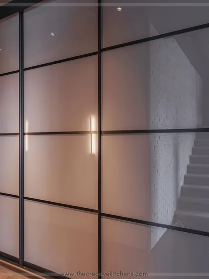 A close-up of the black profile grid on the back-painted glass shutters. This detail adds a subtle graphic element to the minimalist design, breaking up the large surface area with understated elegance.