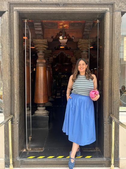 Standing at the entrance of The Spice Route. My outfit, with its pop of blue and pink, contrasts beautifully with the dark, carved wood of the doorway.