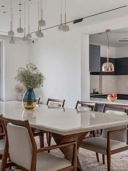 We specialize in creating cohesive, open-plan living areas. This view shows how the elegant dining space, with its onyx tabletop and statement lighting, flows seamlessly into a modern, minimalist kitchen. This approach enhances natural light and creates a perfect environment for family life and entertaining.