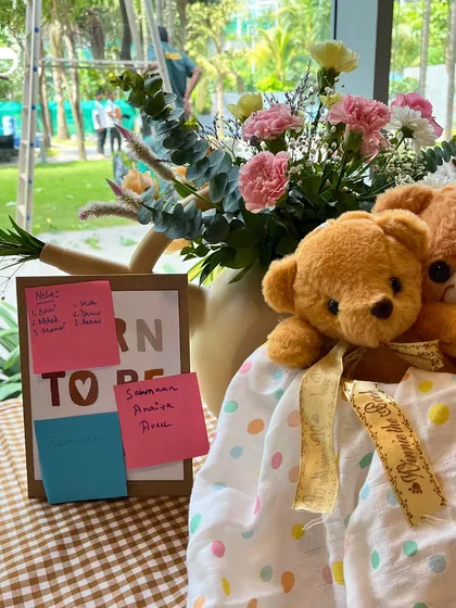 A "Born to be Loved" sign is covered in name suggestions from guests, sitting next to a basket of adorable teddy bears. This corner is full of love and anticipation.