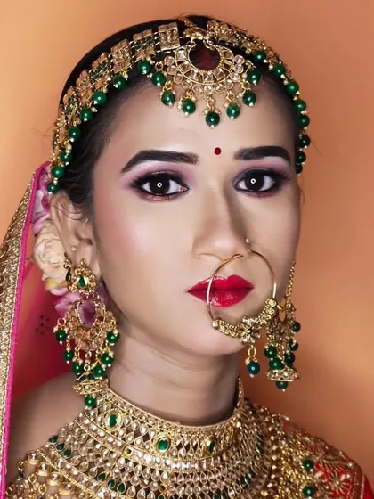 A stunning close-up of a bride with sharp, defined features, a red lip, and beautiful green beaded jewellery.