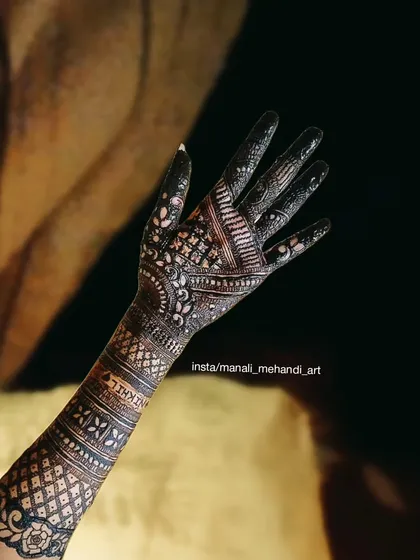 A beautiful example of an Arabic-style mehandi design on the back of the hand. The pattern uses bold lines, delicate shading, and negative space to create a flowing, elegant look.