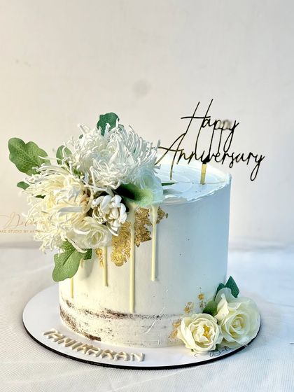 A rustic-chic anniversary cake. This semi-naked cake features a white chocolate drip and is topped with a beautiful bouquet of white flowers and greenery.