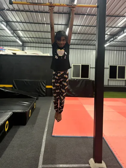 A young gymnast shows her strength and a happy smile while practicing bar hangs.