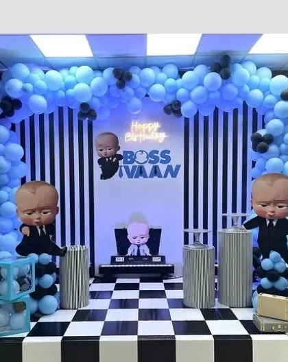 A 'Boss Baby' themed birthday party with a cool blue and black color scheme. The decoration includes character cutouts, a checkered floor design, and a custom neon sign for 'Boss Ivaan'.